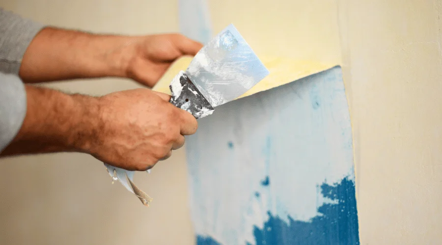 person holding a brush while pulling a strip of paint from the wall
