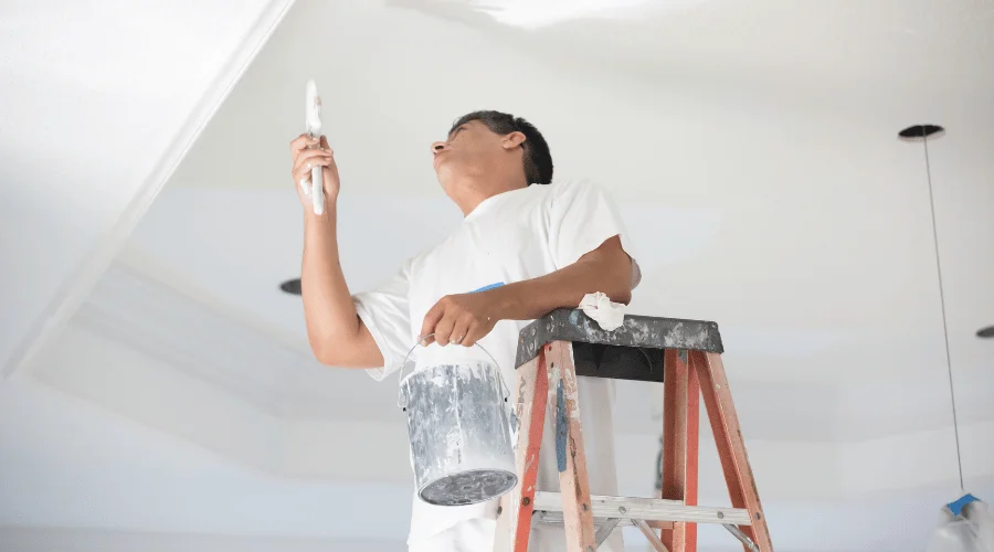 painter on step ladder painting the ceiling